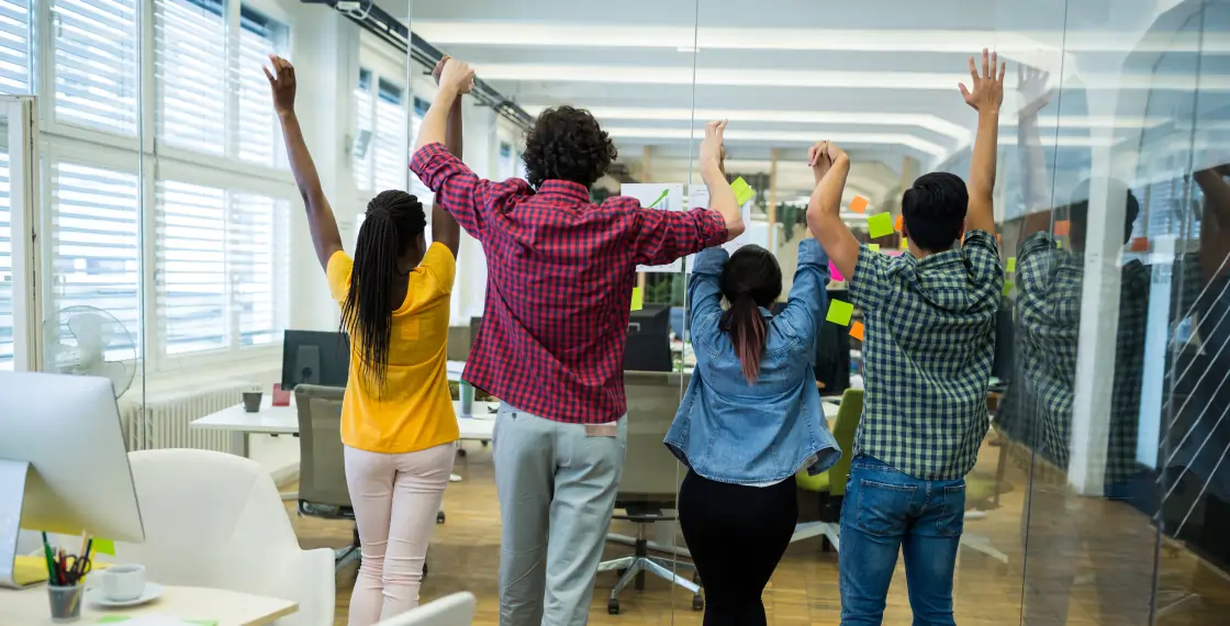 Diverse business team raising their arms together in a modern office space.