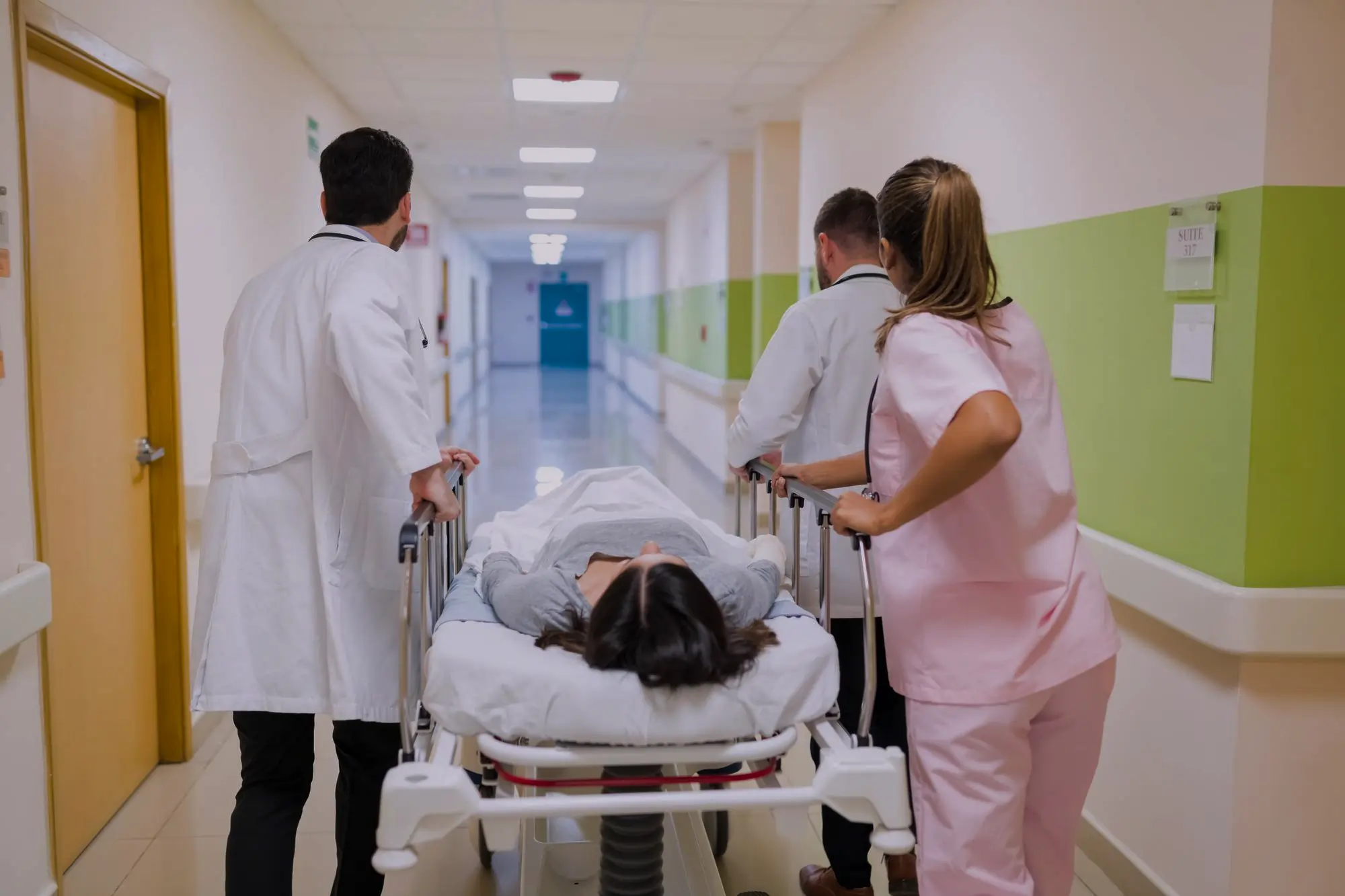 Hospital staff and doctor transporting a patient on a stretcher through a hospital corridor, showcasing Script All DNA’s Hospital Management System in action