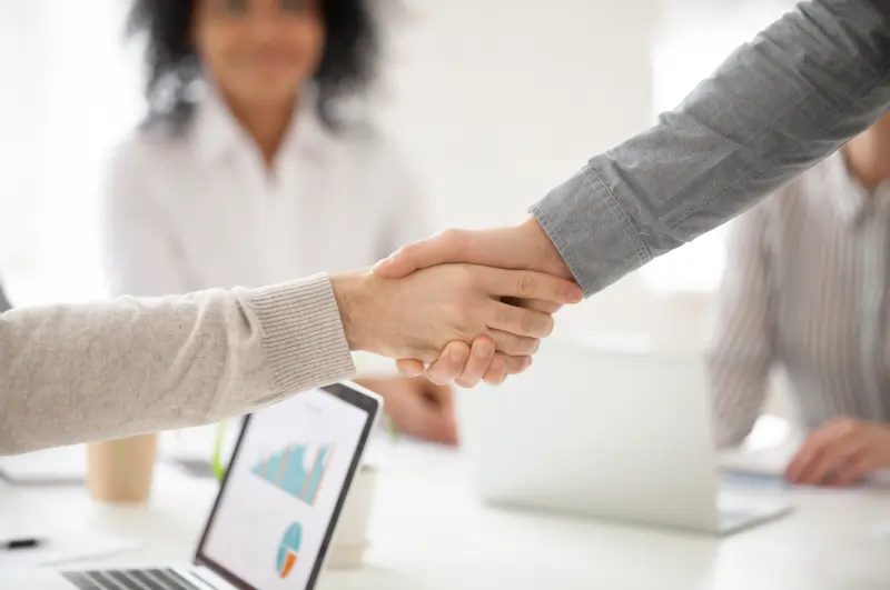 Close-up of two professionals shaking hands over a conference table after a business meeting.