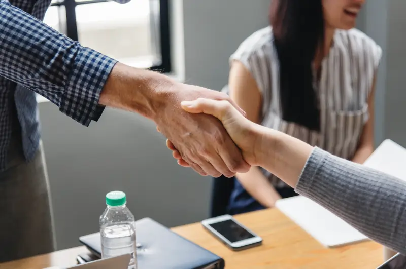 Two business professionals shaking hands over a table with a laptop displaying a growth chart.